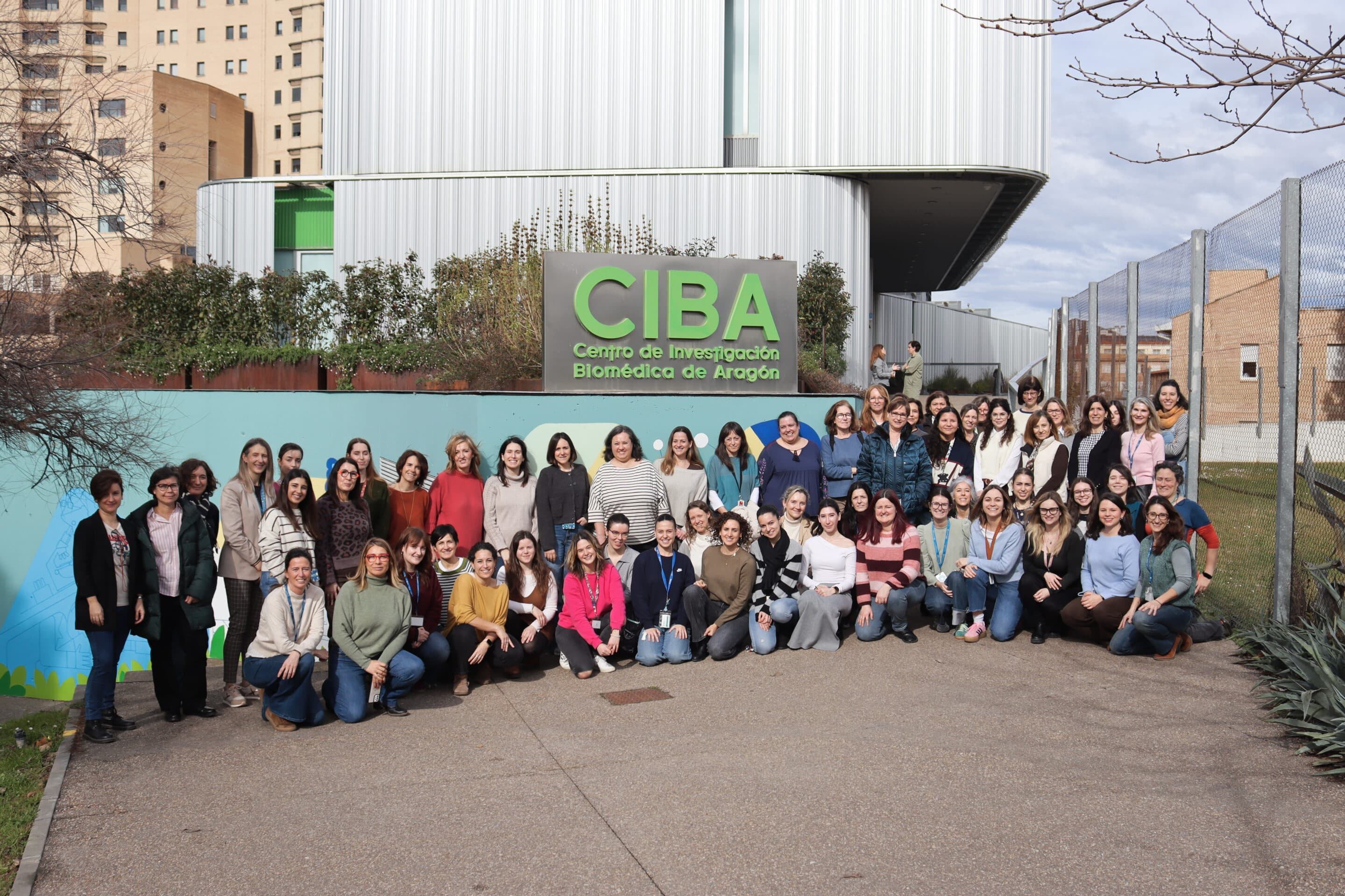 Foto de grupo de las mujeres que trabajan en el Instituto Aragonés de Ciencias de la Salud, por el 11 Febrero 2026, Día Internacional de la Mujer y la Niña en la Ciencia, con el edificio CIBA de fondo